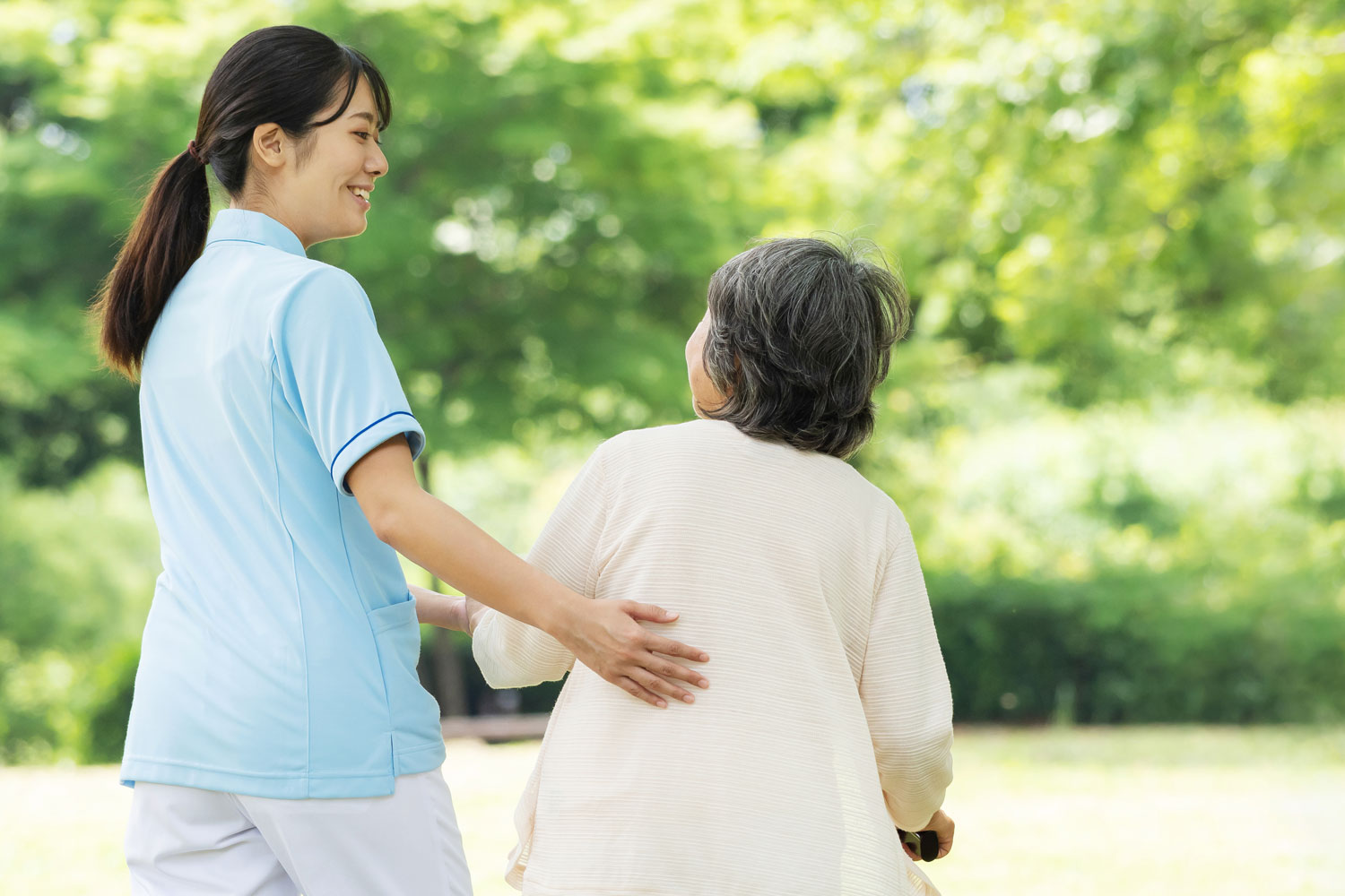 公園を歩く高齢者と介護士の後ろ姿